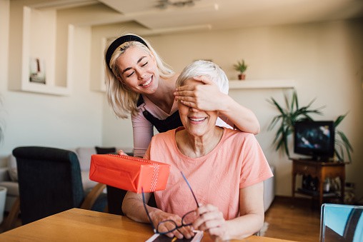 Older woman receiving a surprise from her happy daughter | gifts for mom from daughter