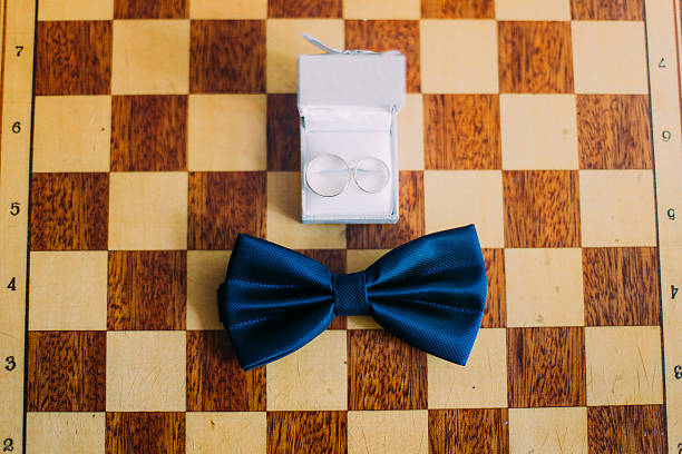 Wedding rings in white box along with bow-tie lie on chessboard. Close up shot of groom's accessories. _wedding gifts for board game lovers