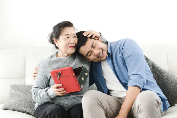 Happy Asian man giving gift box to his mother for Mother's Day celebration. _ asian mom gifts
