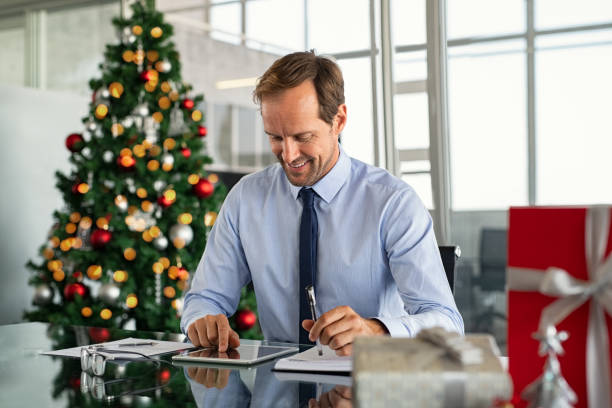 Mature business boss working with digital tablet with xmas present and gift on desk. Successful formal businessman using digital tablet to send an email while sitting in modern office. Happy entrepreneur working in office during Christmas holiday. _christmas gift for a boss