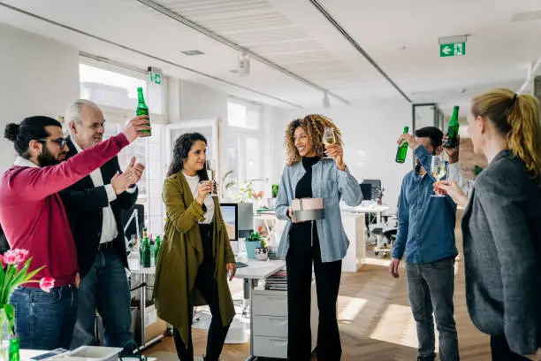 Business people having a party at office. Multi-ethnic business people raising beer bottles and wineglasses during a farewell party of a teammate at work _ farewell gifts for a teammate