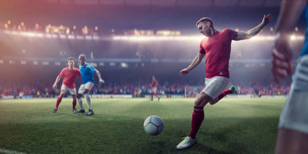 A professional male soccer player with foot back and arms out about to kick football in a volley during a soccer match. The player is dressed in generic red and white soccer kit and is near other players who are playing in a game on a generic outdoor soccer pitch. _soccer senior night gifts