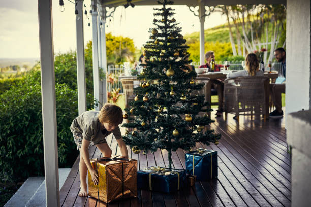 Shot of a little boy picking up his gift under the Christmas tree in his patio - gift ideas for patio lovers