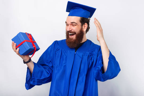 Amazed student man in blue bachelor holding gift box. - gift ideas for a doctoral graduate