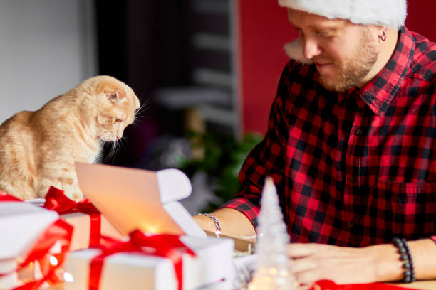 Vet Man in Santa hat and cat in hand making greeting card for New Year and Christmas, congratulation for clients or friends or family , packing presents or gifts, mail manager concept. - cat dad father’s day gifts