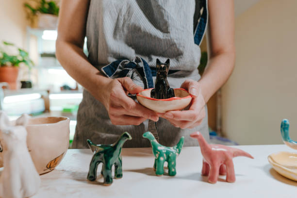 Young woman ceramist holding small colorful ceramic dinosaur figurines in the workshop. Close up, selective focus. - clay father’s day gifts